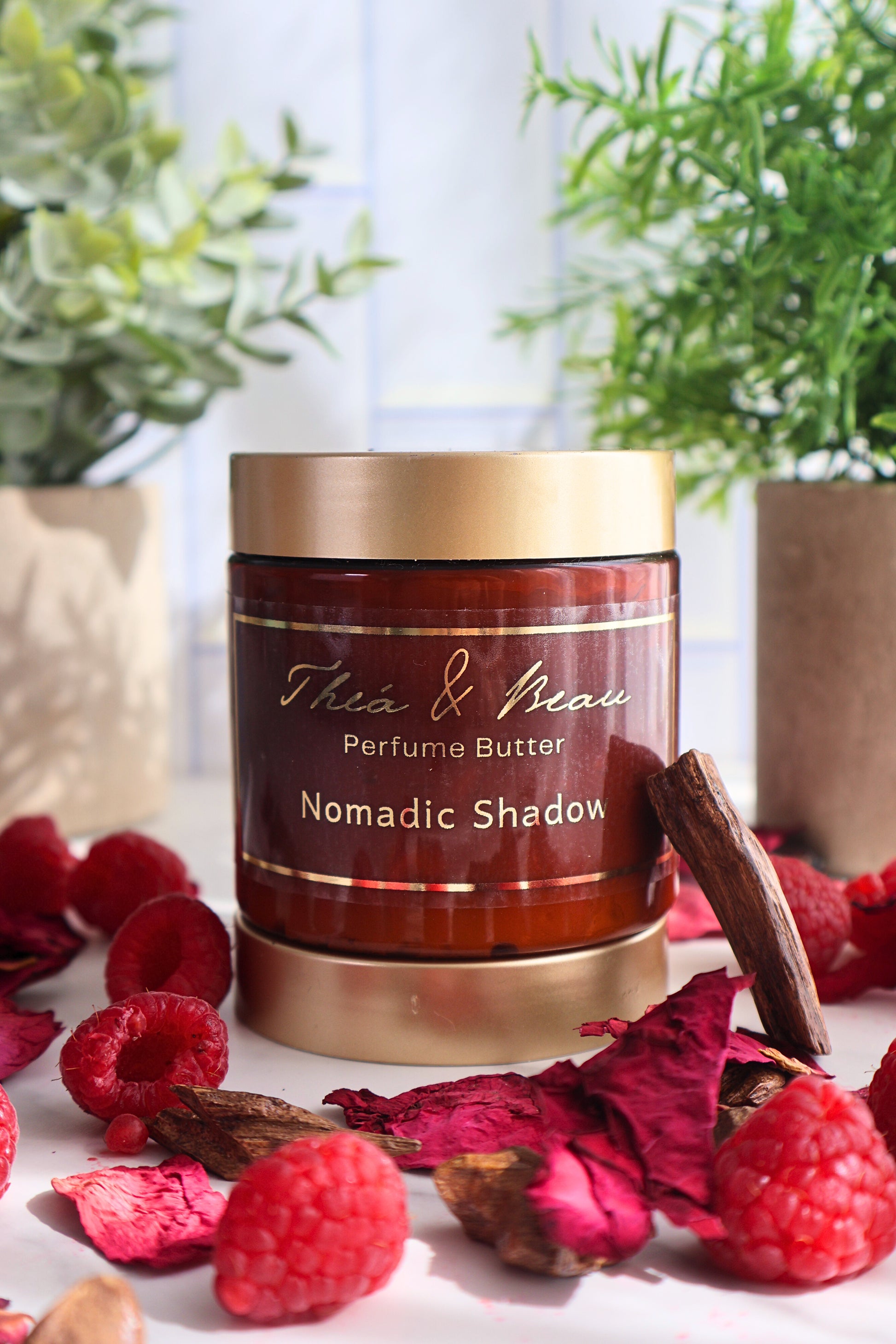 Nomadic Shadow perfume body butter in our luxury jar on white surface with raspberries rose petals and oud accents