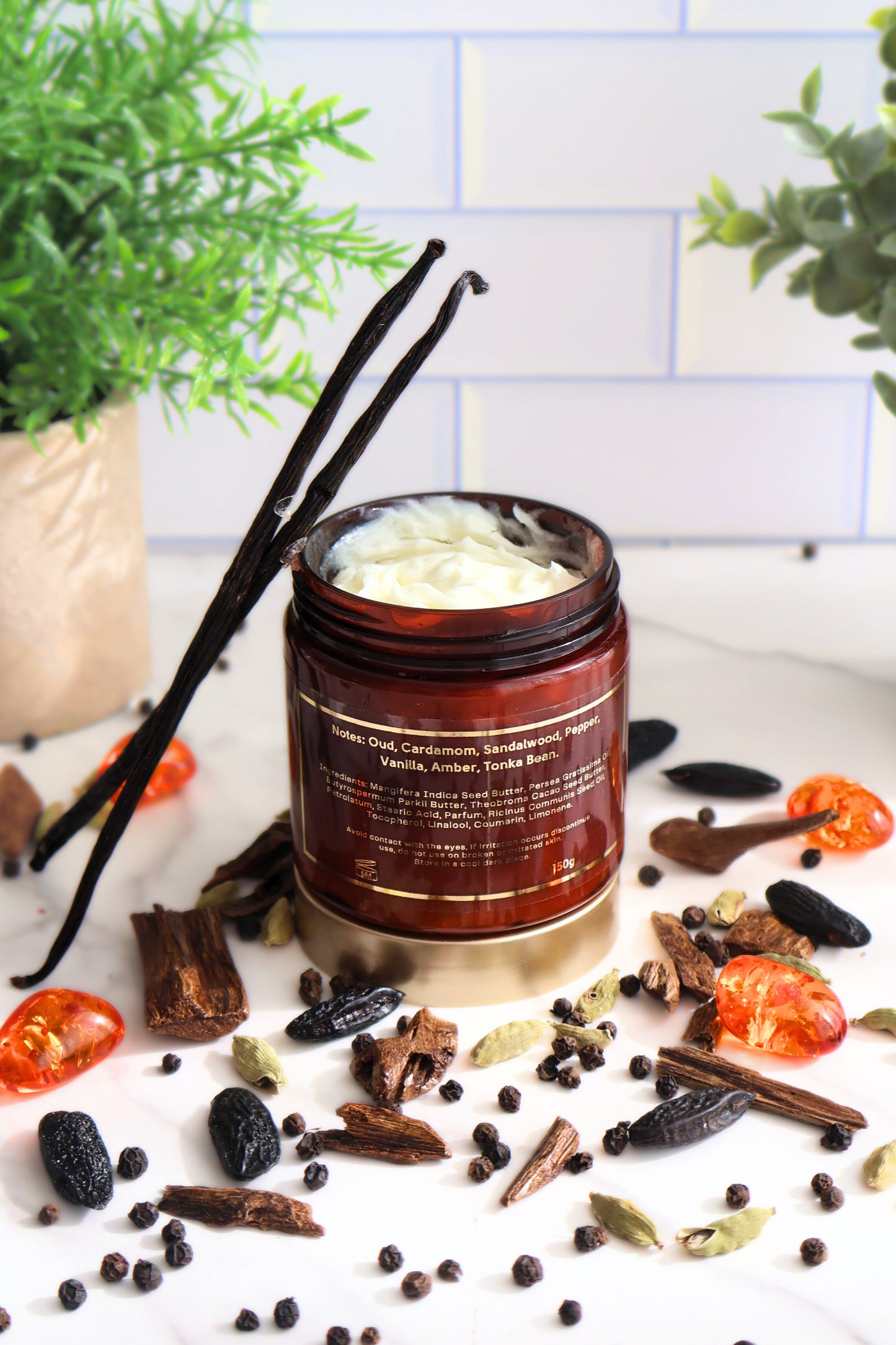 Close-up of Woody Oud perfume body butter showing back of jar on white surface with vanilla and oud accents